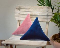 two blue and pink pillows sitting on top of a wooden bench next to a potted plant