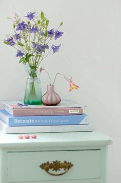 a stack of books sitting on top of a table next to a vase filled with flowers