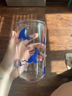 two hands holding up a glass with blue fish painted on it