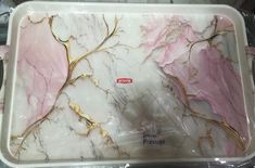 a white and pink marble serving tray with gold leaf designs on the side, sitting on top of a plastic wrapper