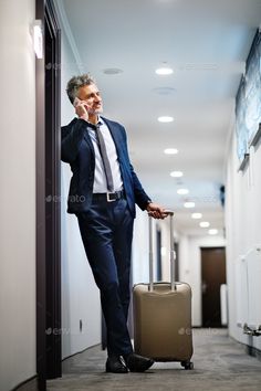 a man is talking on his cell phone while walking down the hallway with a suitcase