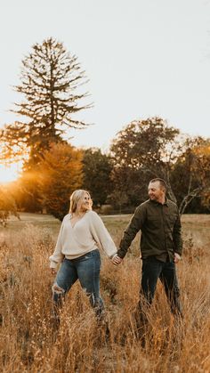 a man and woman holding hands walking through tall grass in an open field at sunset