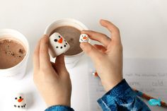 someone is holding two dice shaped like snowmen in front of a cup of coffee