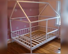 a white wooden bed frame in a room with pink walls and wood flooring,