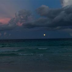 the sun is setting over the ocean with dark clouds in the sky and some blue water