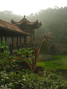 a bridge in the middle of a lush green field with trees and bushes surrounding it