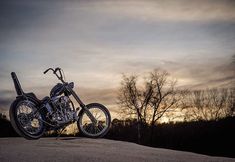 a motorcycle is parked on top of a hill at sunset with trees in the background