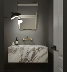 a bathroom sink with a marble counter top and gold faucet light above it