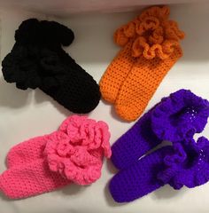 four pairs of crocheted slippers are shown in different colors and sizes, one is pink, the other is purple