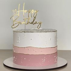 a white and pink birthday cake with gold happy birthday topper on a plate that says happy birthday