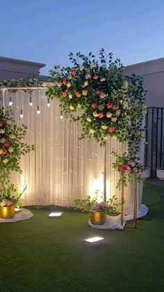 an outdoor wedding setup with flowers and greenery on the wall, lights in the background