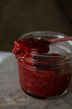 a jar filled with ketchup sitting on top of a wooden table next to a spoon