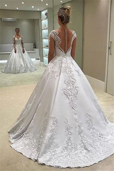 a woman in a white wedding dress looking at herself in the mirror with her back to the camera