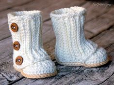 a pair of white knitted boots with buttons on the bottom and side, sitting on a wooden surface