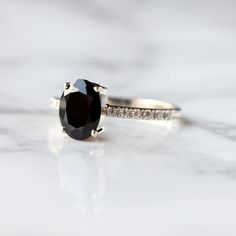 an engagement ring with a black diamond in the center on a white marble countertop