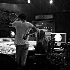 a man standing next to a woman in front of sound mixing equipment at a recording studio