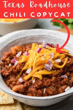 a bowl filled with chili and cheese next to crackers