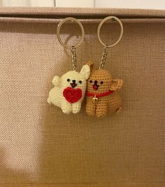 two crocheted teddy bears holding a heart shaped keychain