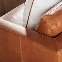 a brown leather couch with two pillows on it's back and the arm rest