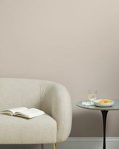 a chair and table with a book on it next to a glass vase filled with oranges