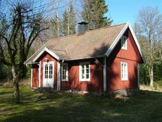 a small red house sitting in the middle of a green field next to some trees