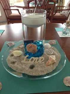 a plate with sand and seashells on it next to a glass of water