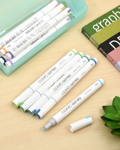 four markers and three pens sitting on top of a wooden table next to a green plant