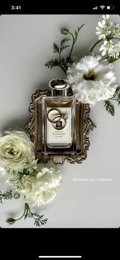 a bottle of perfume sitting on top of a table next to white flowers and greenery