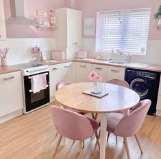 a kitchen with pink chairs and white cabinets is pictured in this image, the table has a laptop on it