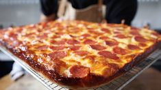 a large pepperoni pizza sitting on top of a metal rack next to a person