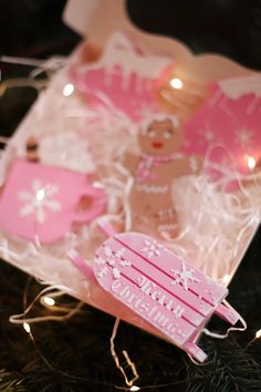 a pink christmas ornament in a box with lights on the side and a teddy bear inside