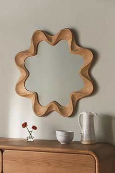 a mirror sitting on top of a wooden dresser next to a white vase and flower