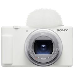 a white digital camera with a furry ball on the top of it's lens