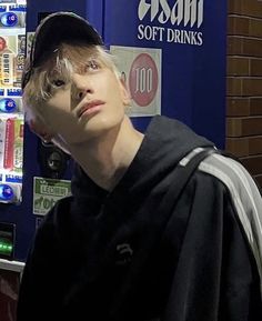 a young man standing in front of a vending machine with his head covered by a cap