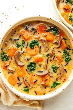 two bowls of soup with carrots, mushrooms and spinach on the side next to a napkin