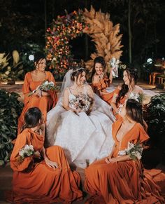 a group of bridesmaids in orange dresses sitting on the ground