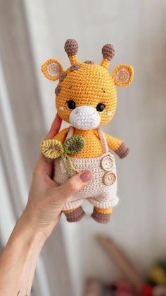 a hand holding a small crocheted giraffe stuffed animal with leaves on it's tail