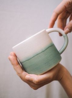 a person holding a coffee cup in their hands with the handle extended to show it's color