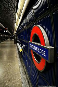 the london bridge sign is attached to the wall in the subway station, with people walking by