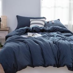 a bed with blue comforter and pillows in a room next to a window,