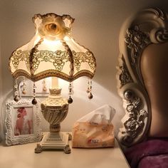 a lamp sitting on top of a white table next to a chair and pictures in frames