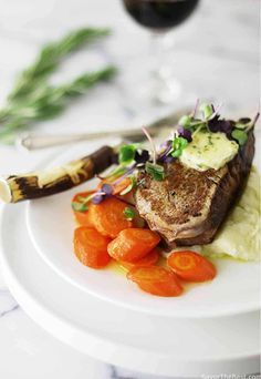 a white plate topped with meat and veggies next to a glass of wine