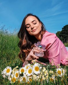 a woman laying in the grass with daisies around her and holding a small jar