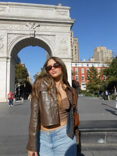 a woman standing in front of an arch on a sunny day with her hands in her pockets