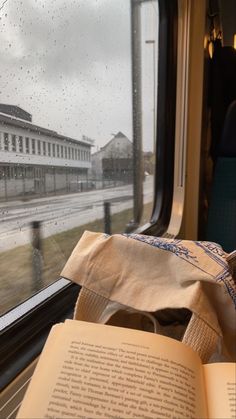 an open book sitting on top of a table next to a window with raindrops