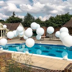 white balloons floating in the air over a swimming pool surrounded by brick buildings and trees