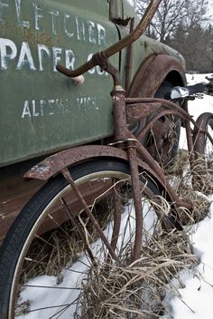 an old rusty bicycle is parked next to a green truck with writing on the side