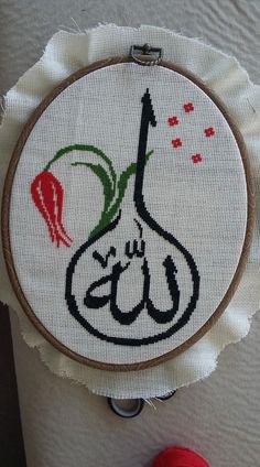 a cross stitched wall hanging with an arabic calligraphy on it and a red ball of yarn next to it