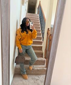 a woman taking a selfie while standing in front of stairs with her handbag