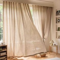 a living room filled with furniture and a large window covered in draping next to a book shelf